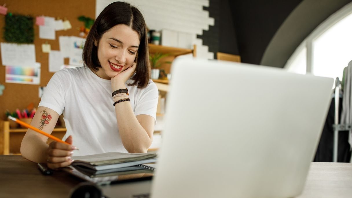 Young woman following online class and taking notes