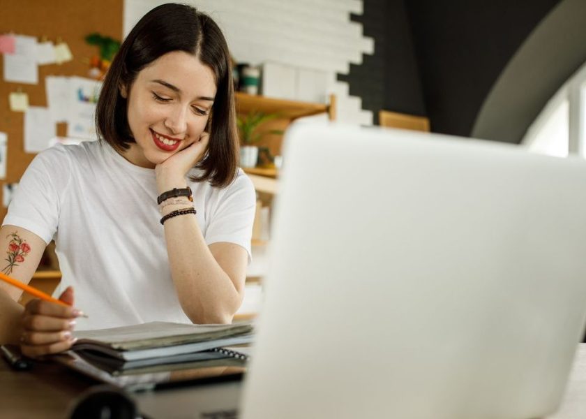 Young woman following online class and taking notes