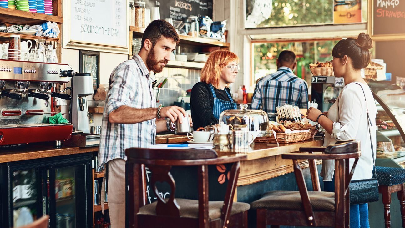 Barista, woman and cafe as waitress in small business with customer in restaurant or coffee shop. Working people, cafeteria and client for food service with entrepreneur in startup