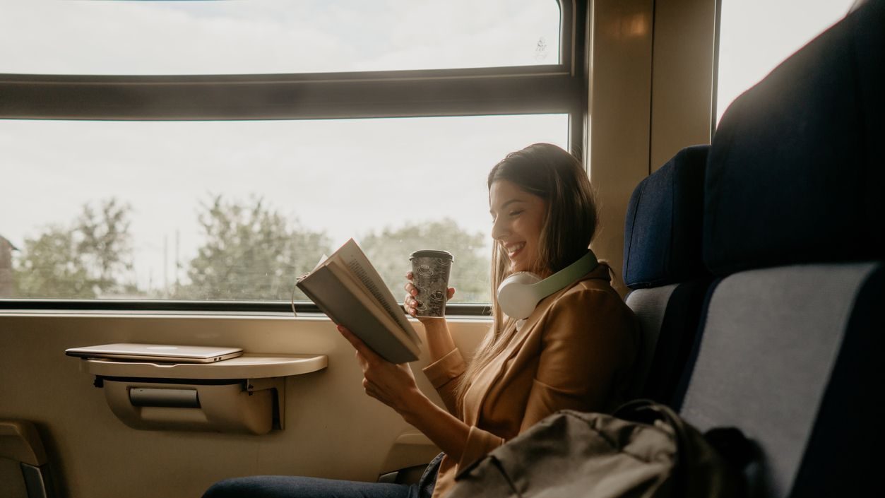 young woman travels by train, wear headphones and reading book